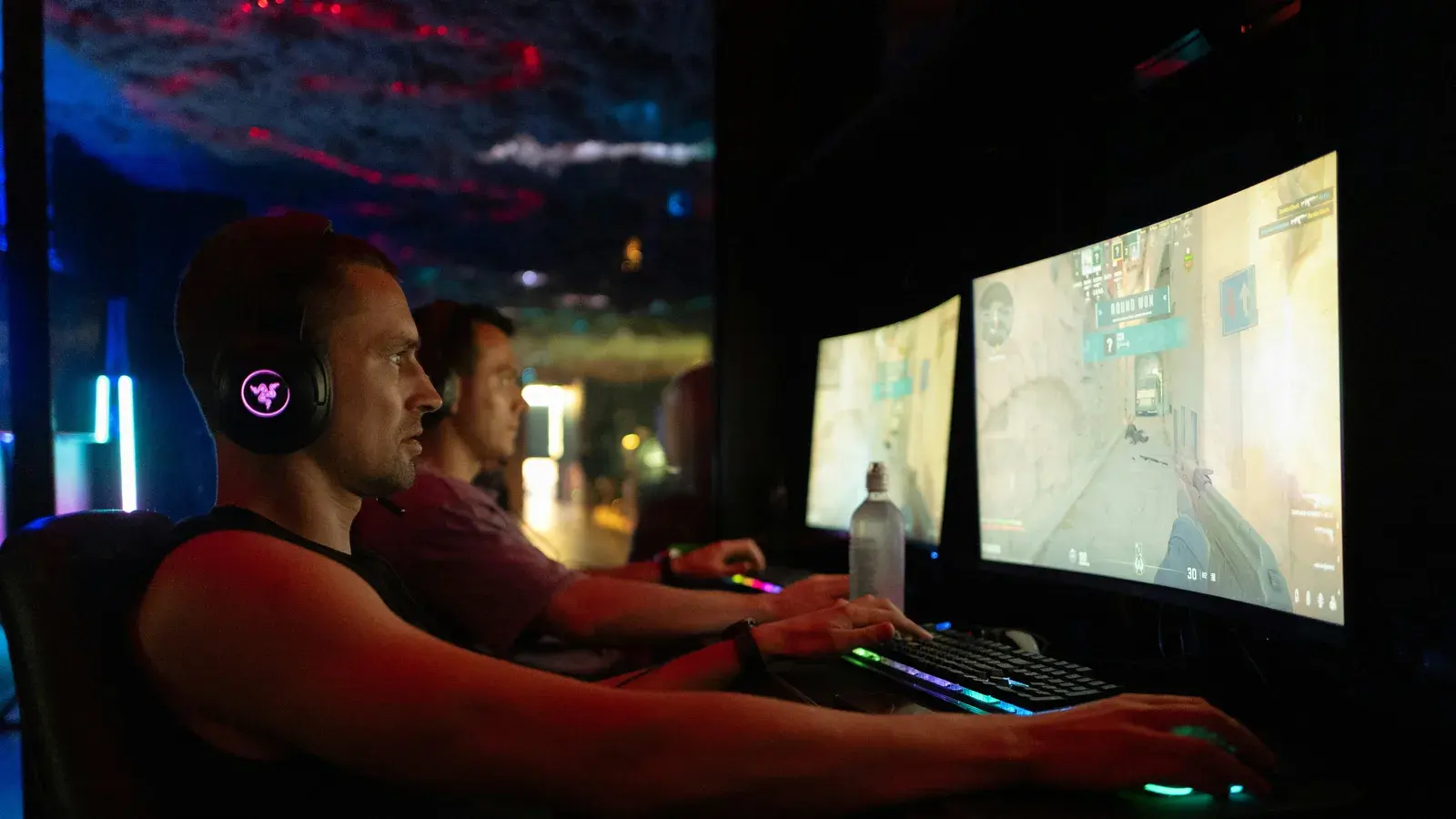 Player in a headset at a two-monitor desk, city lights behind