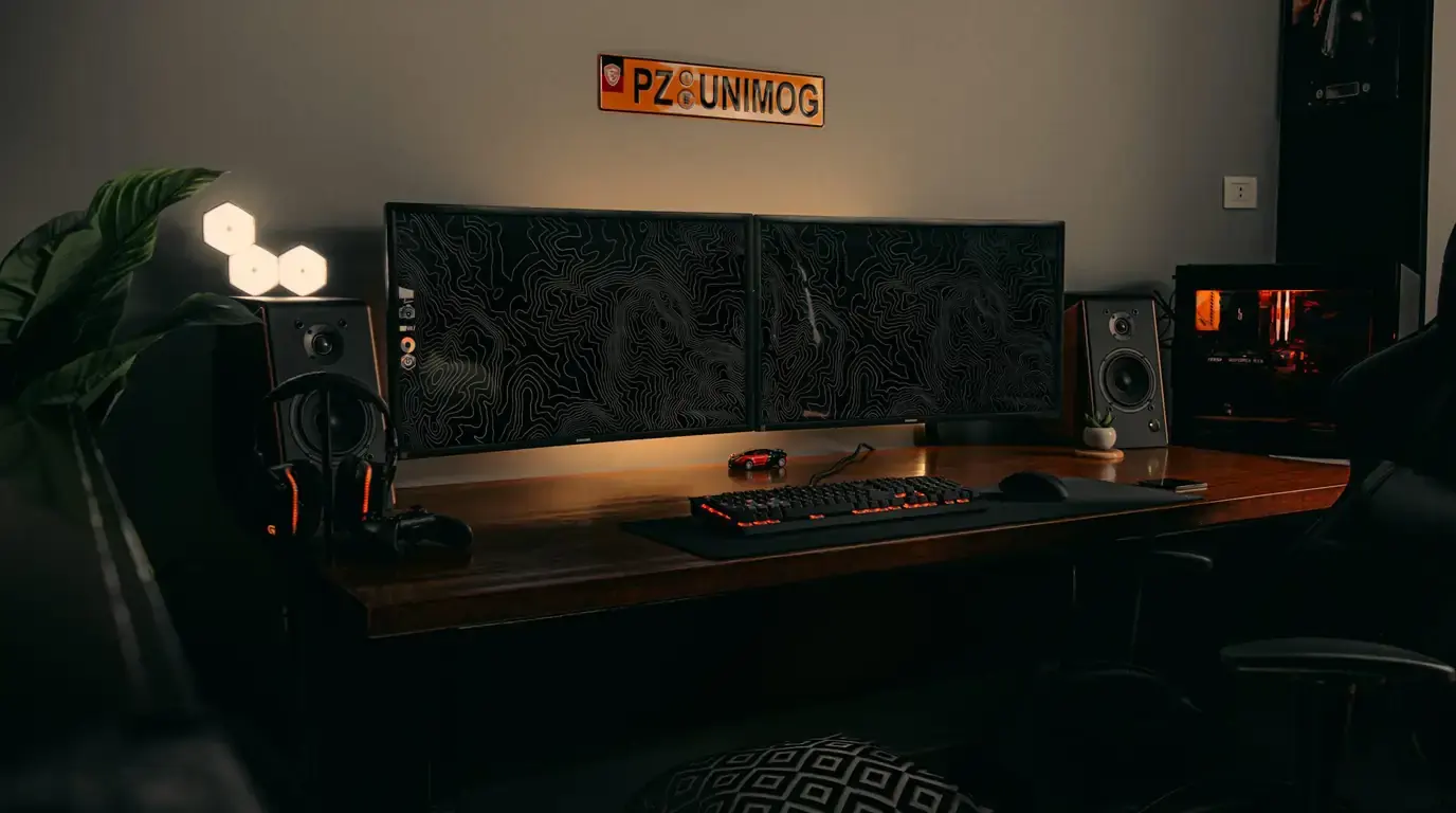 Dark desk setup with triple monitors, bookshelf speakers and keyboard