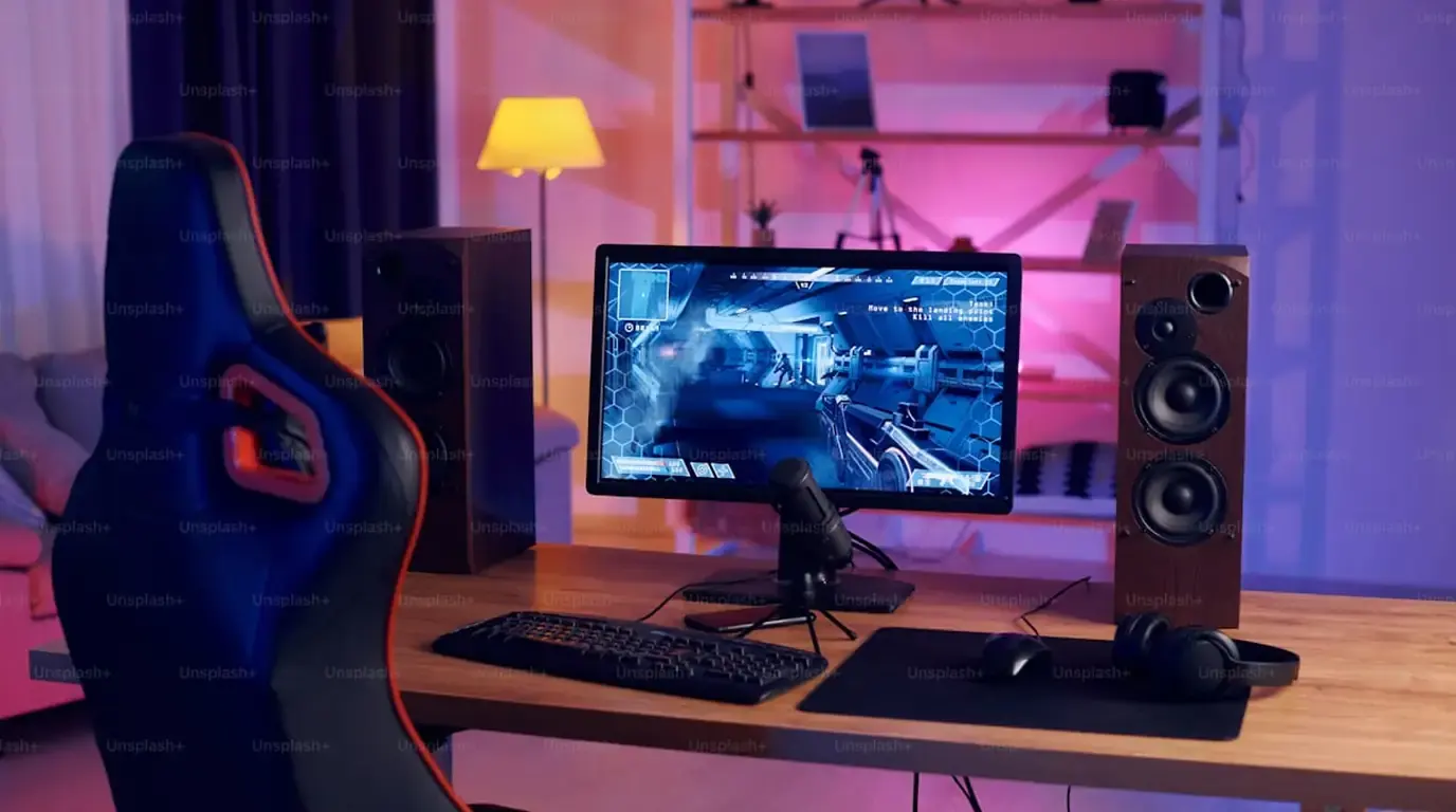 Gaming desk with monitor, racing chair and speakers under pink lamplight