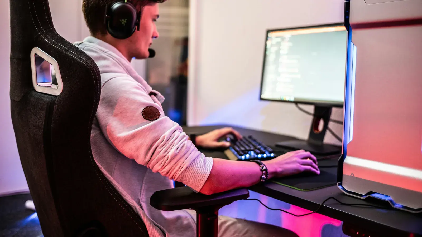 Young man in a headset leaning over a keyboard beside a monitor