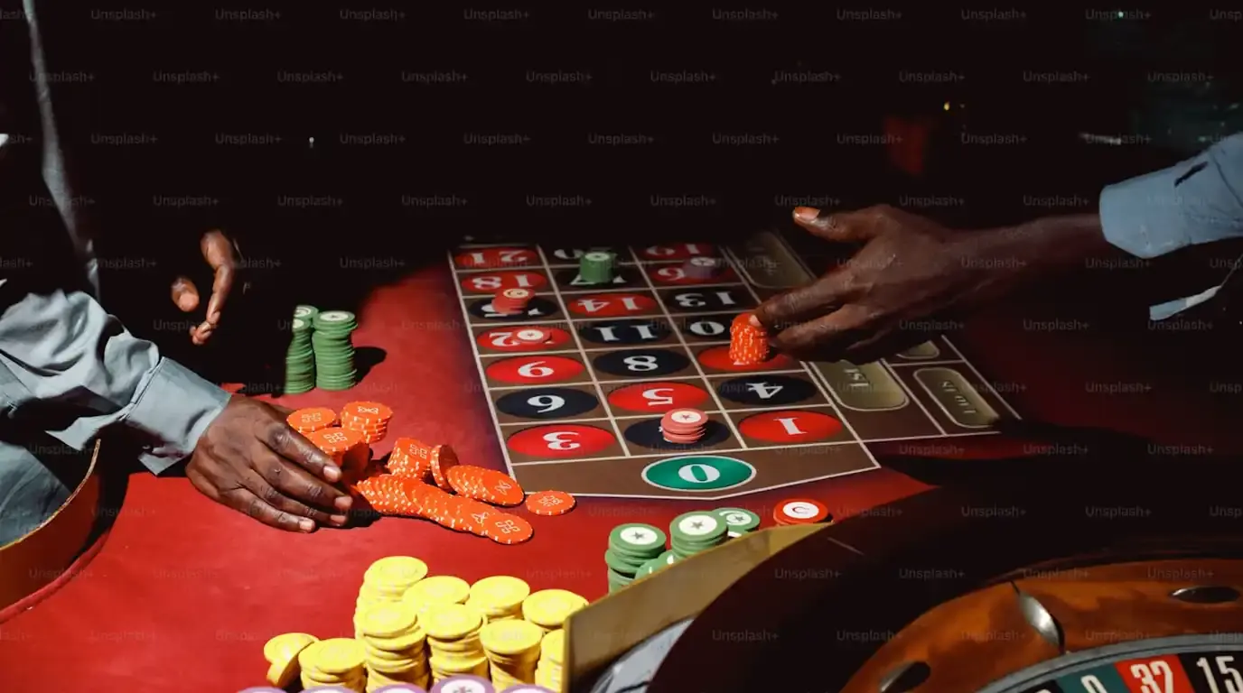 Hands pushing orange chips across a red roulette betting layout