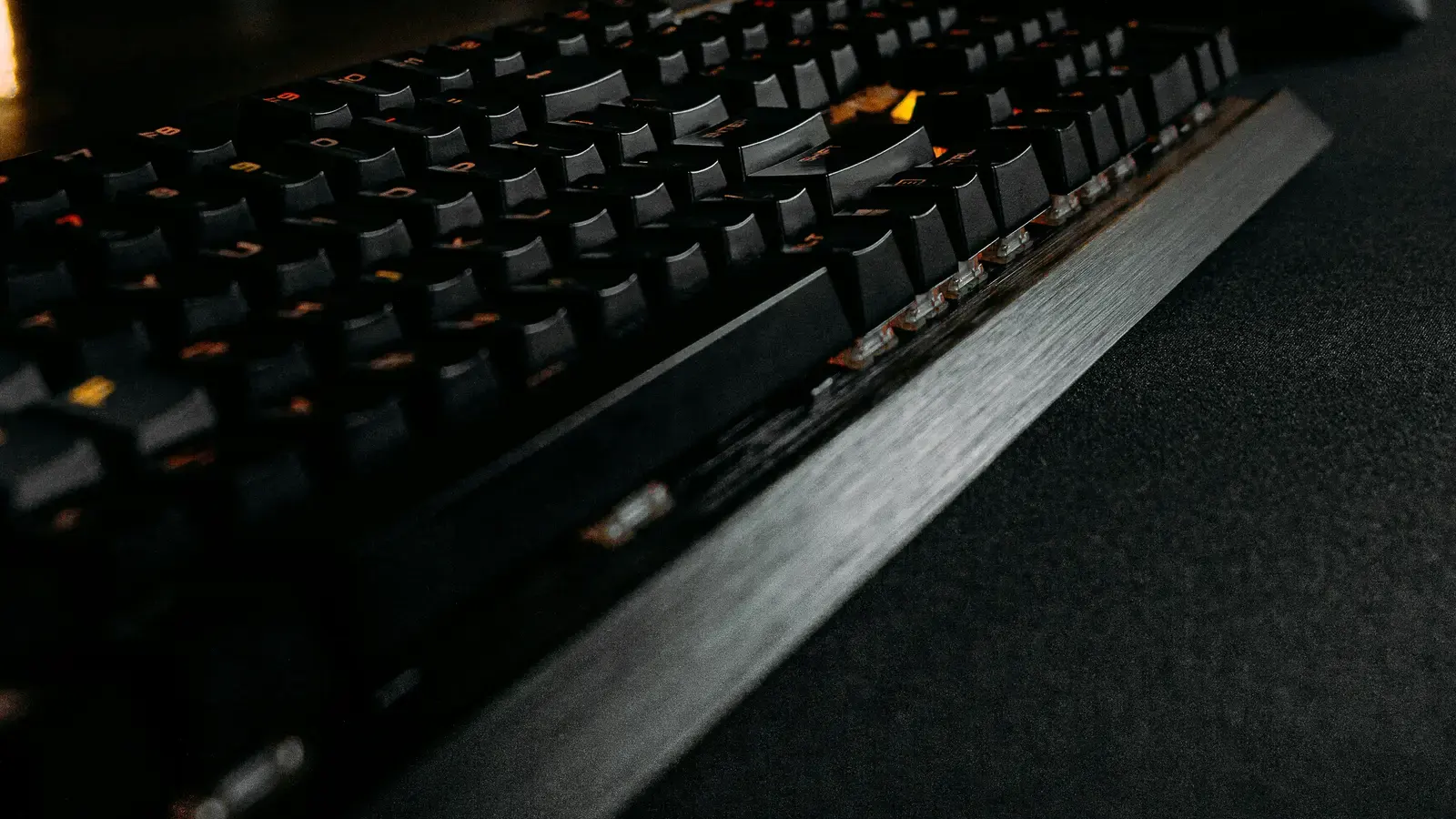 Backlit mechanical keyboard on dark wood, shot along the keys