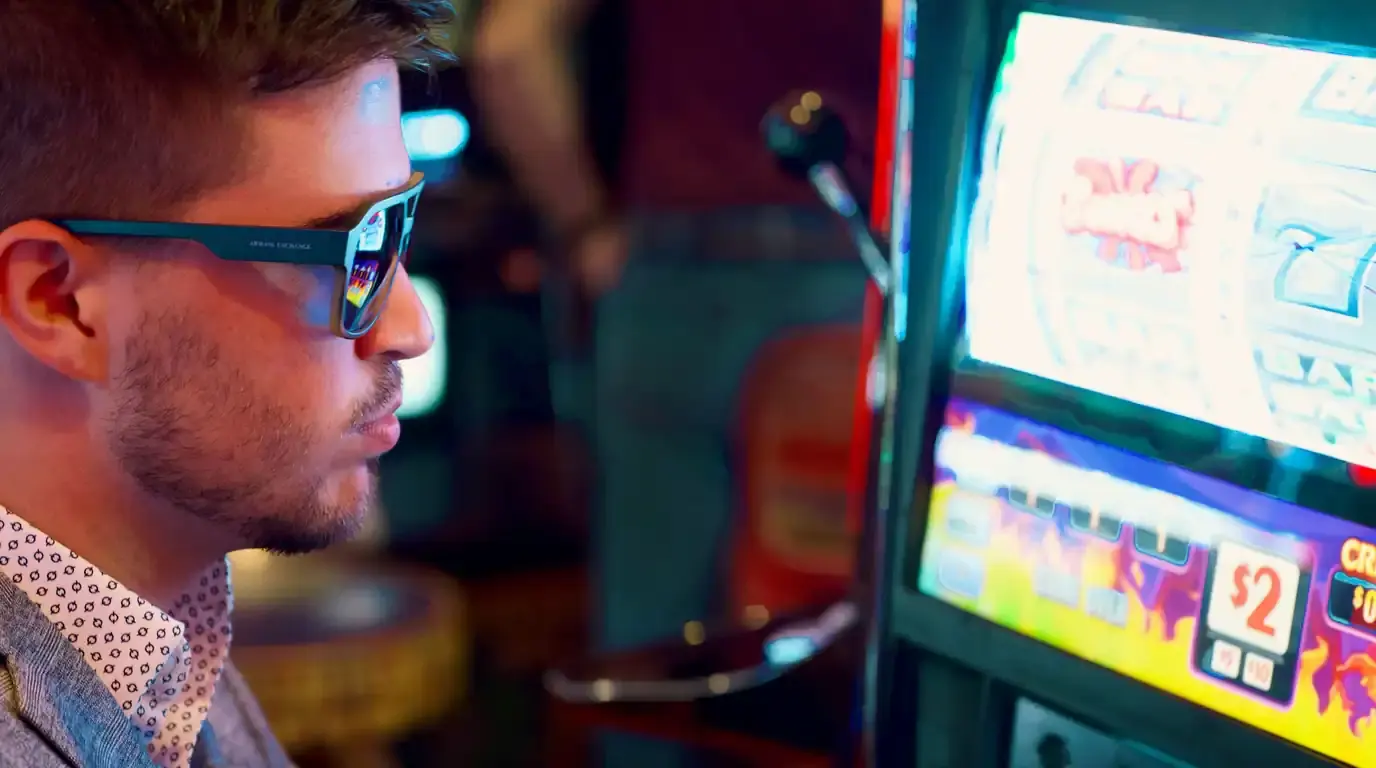 Man in sunglasses in profile beside a brightly lit arcade cabinet