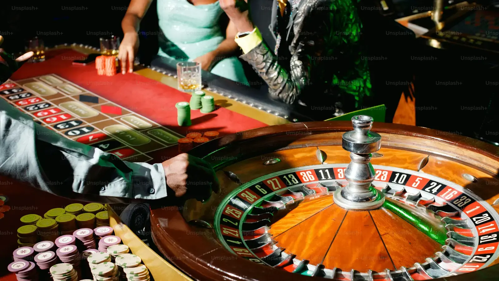 Croupier and players around a roulette wheel stacked with chips
