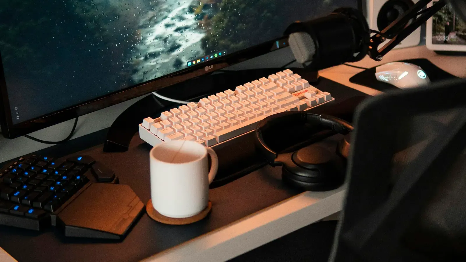 Pale keyboard, mug and headphones on a warm-lit desk