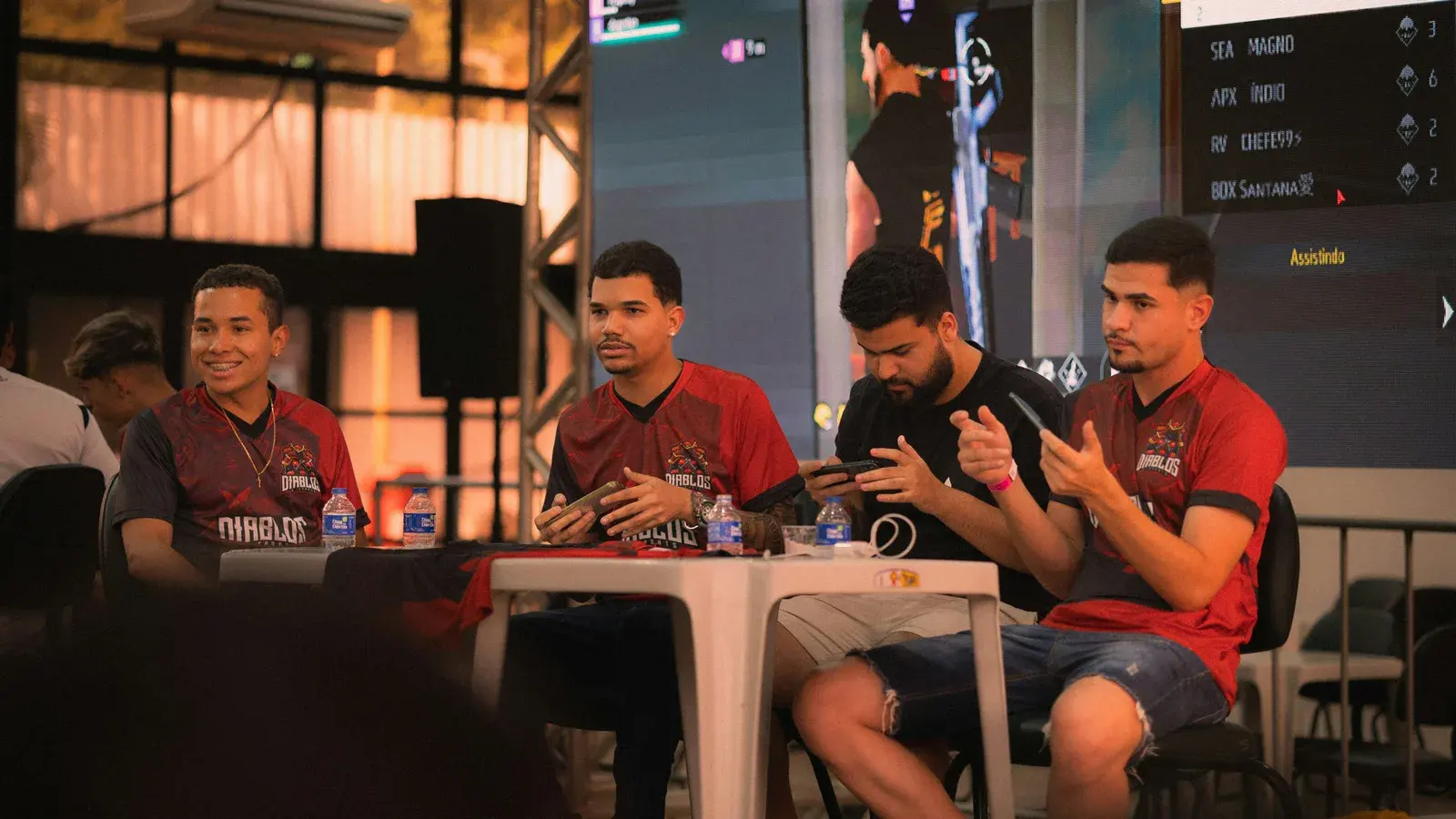 Players in red team jerseys seated along a tournament table