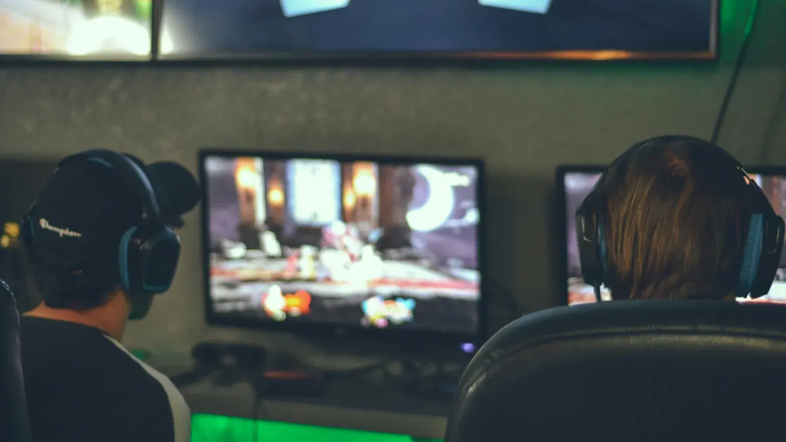 Two players in headsets facing a large screen in a dim room