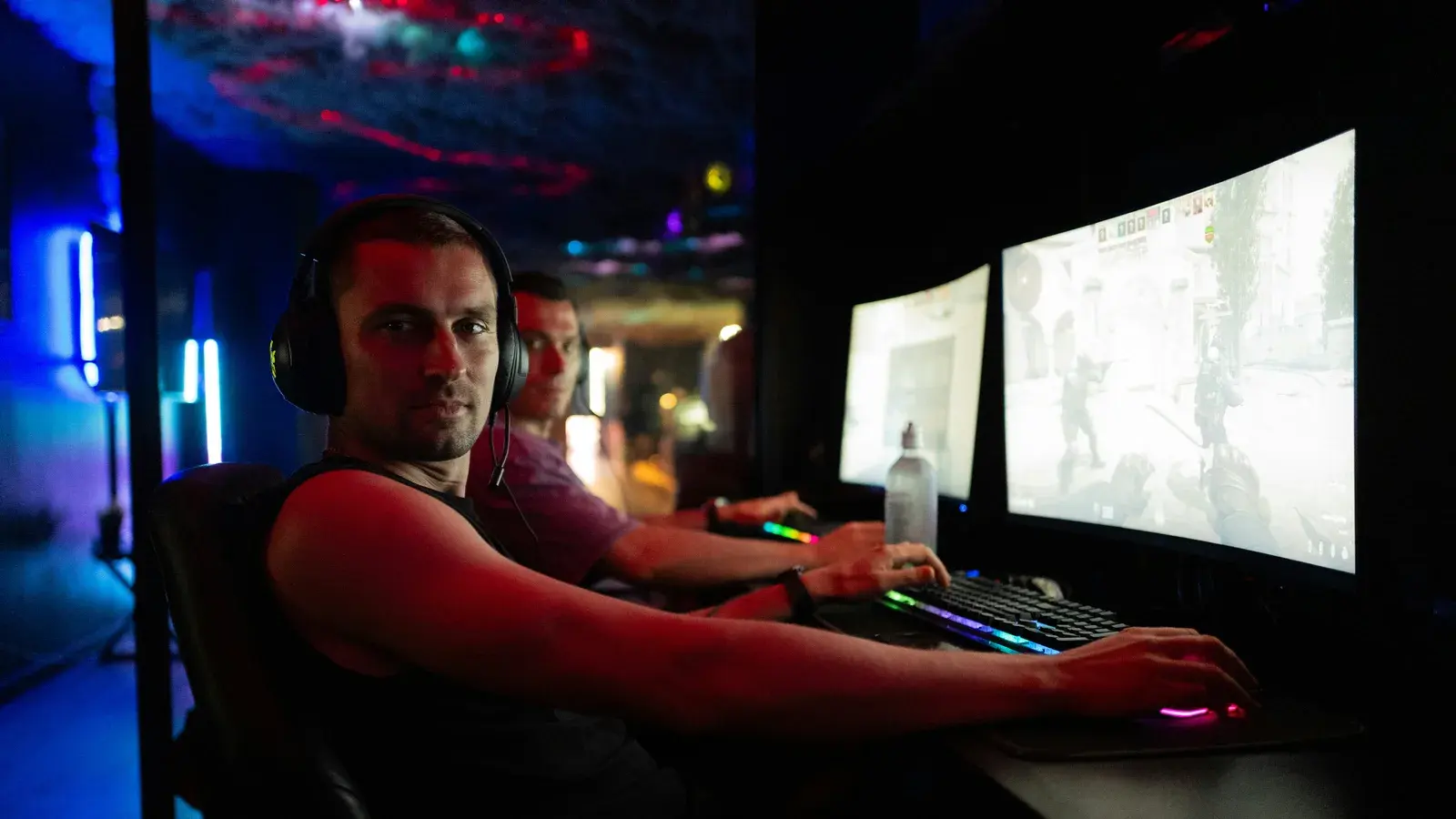 Player leaning back at a two-monitor desk in blue light
