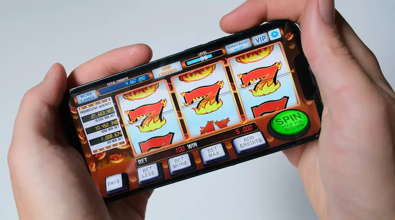 Hand holding a phone showing a slot game with a green spin button