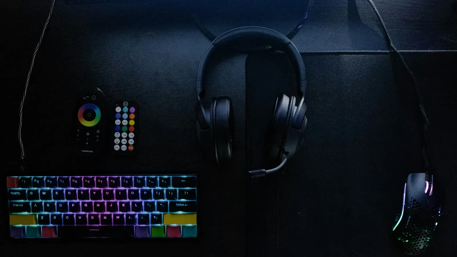 Headset on a hook above a rainbow keyboard on dark felt