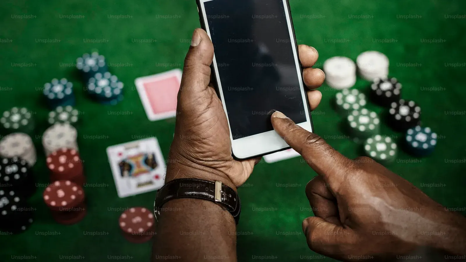 Hands holding a phone over green felt scattered with chips and cards