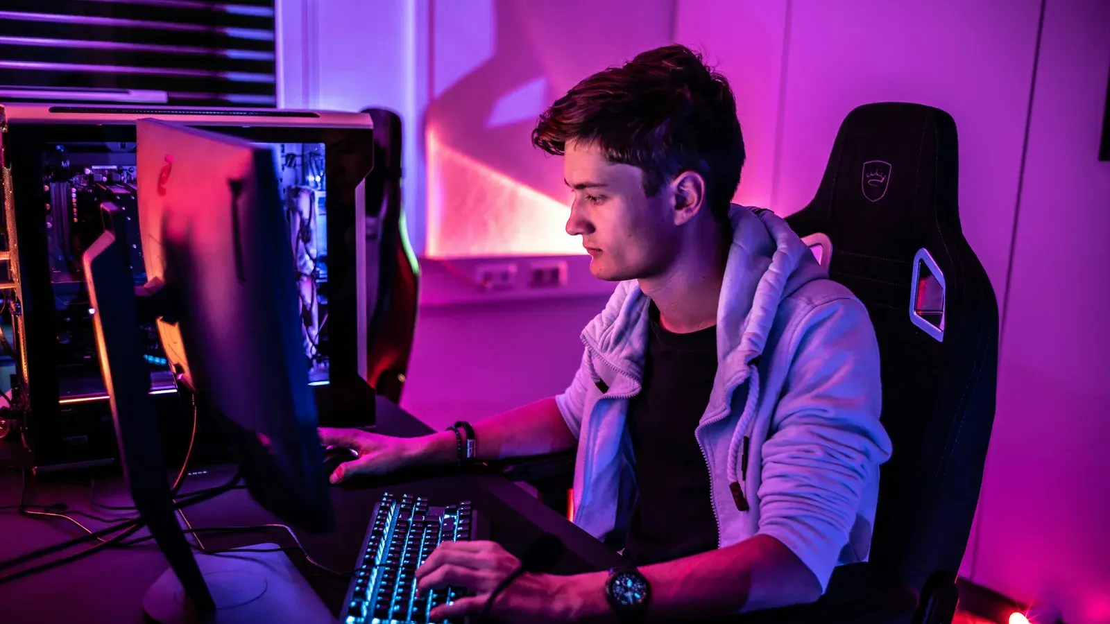 Young man in a hoodie playing at a purple-lit desk