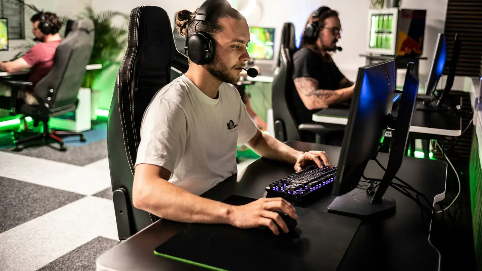 Two men in headsets at monitors in a bright gaming lounge