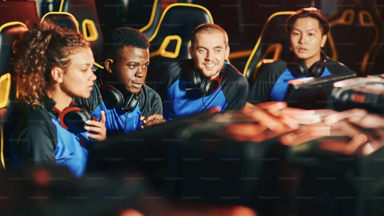 Four teammates in headsets clustered at a desk under orange neon