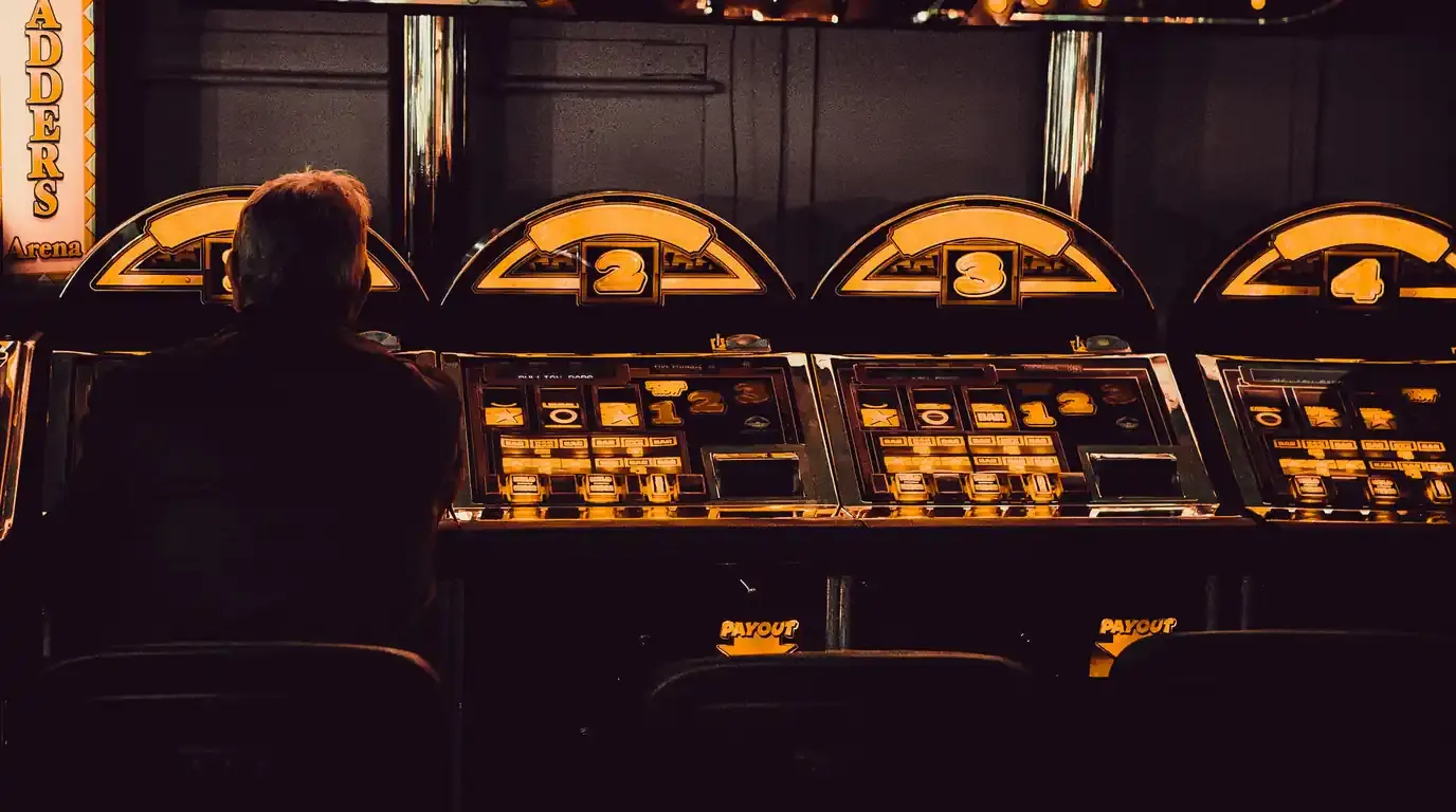 Lone player silhouetted at a row of amber-lit slot machines